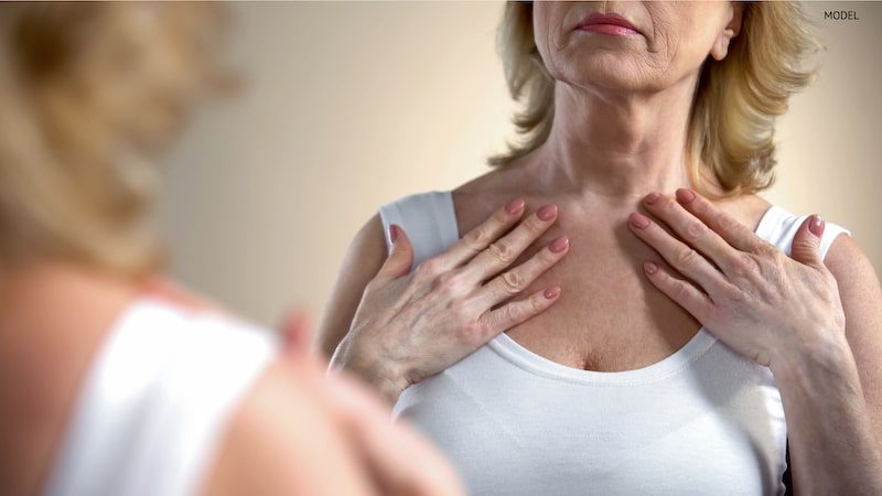 Older woman looking at herself in the mirror, noticing aging signs on her neck and collarbone