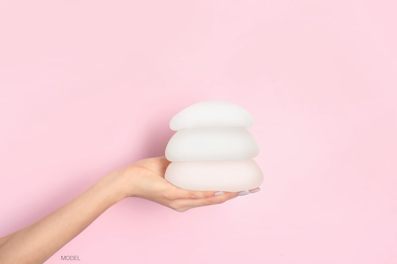 Offscreen woman holding three implants stacked on one another, against a pink background.